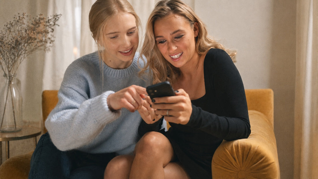 zwei Freundinnen sitzen nebneinander auf der Couch und halten ein Handy in der Hand